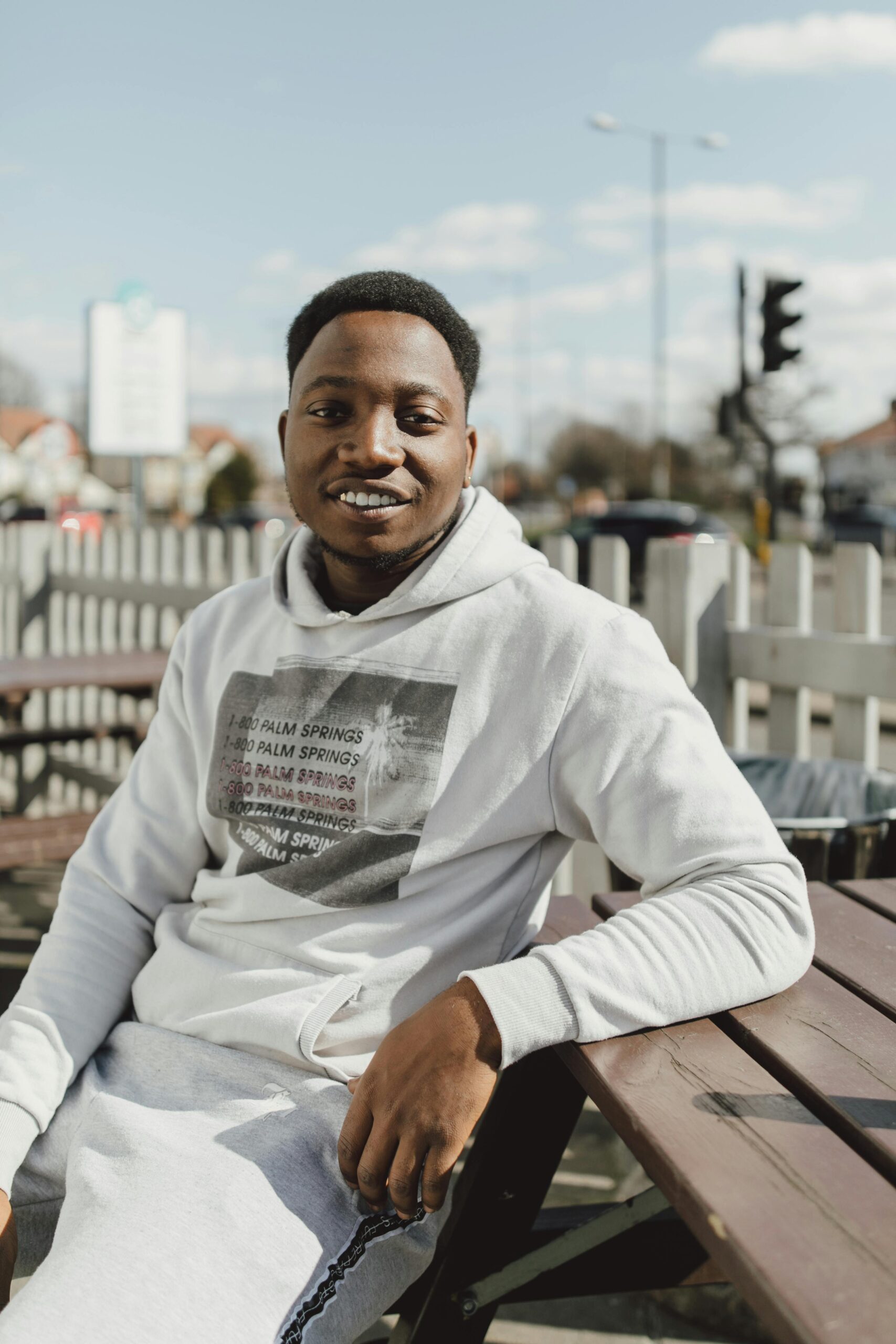 Smiling adult man in a hoodie outdoors, enjoying a sunny day.